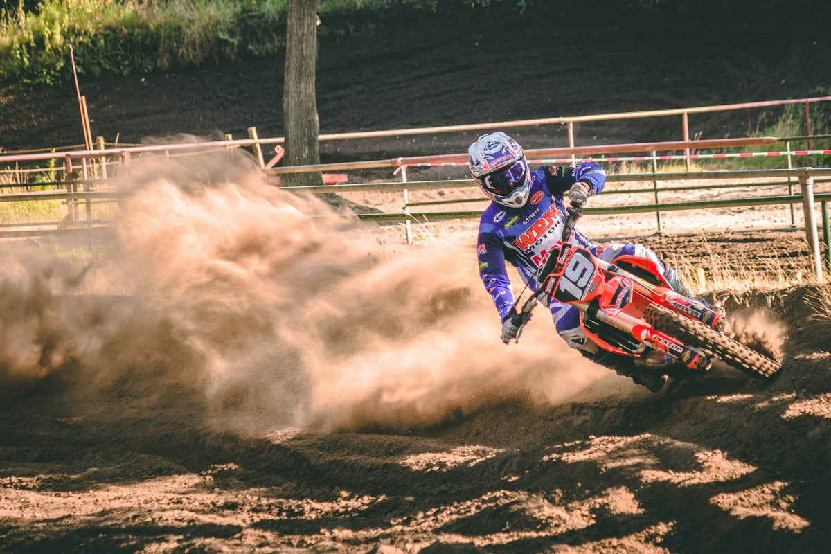 Motocross rider cornering on a dirt track and throwing a trail of dust. Photo by Appic.